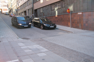 Mehrere Autos auf der rechten Seite einer Straße geparkt, mit Gebäuden mit Fenstern im Hintergrund.