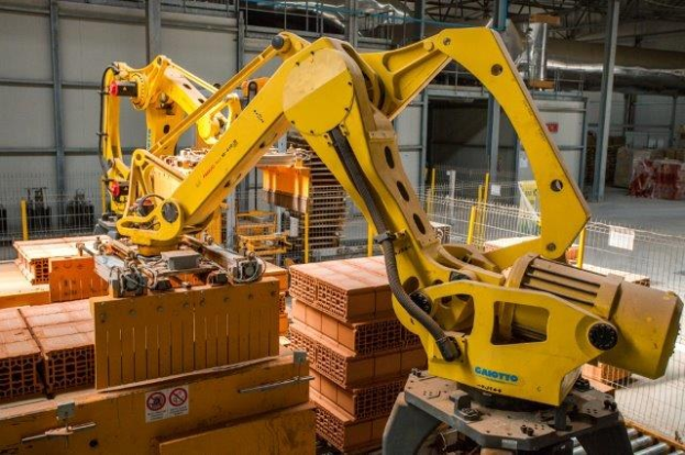 Großes Industriegebäude mit gestapelten Kisten, Kranbrücken, Zaun, Strommasten und einer fernen Wand in einer Fertigungsumgebung.