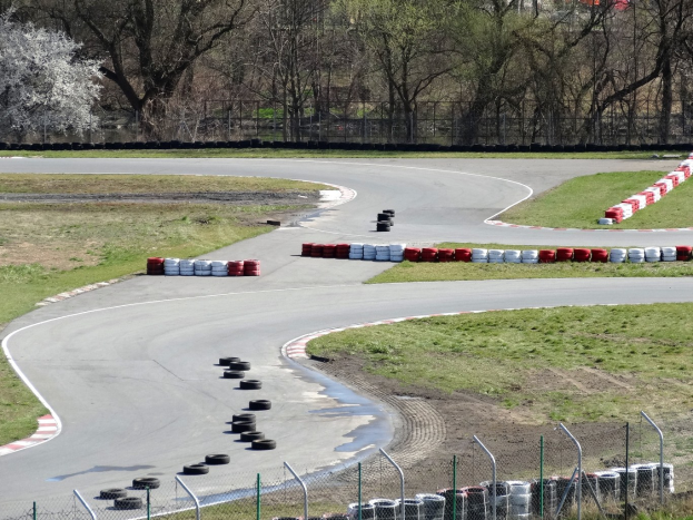 Rennstrecke übersät mit Reifen, gesäumt von Gras und Maschendrahtzaun, mit Bäumen im Hintergrund.