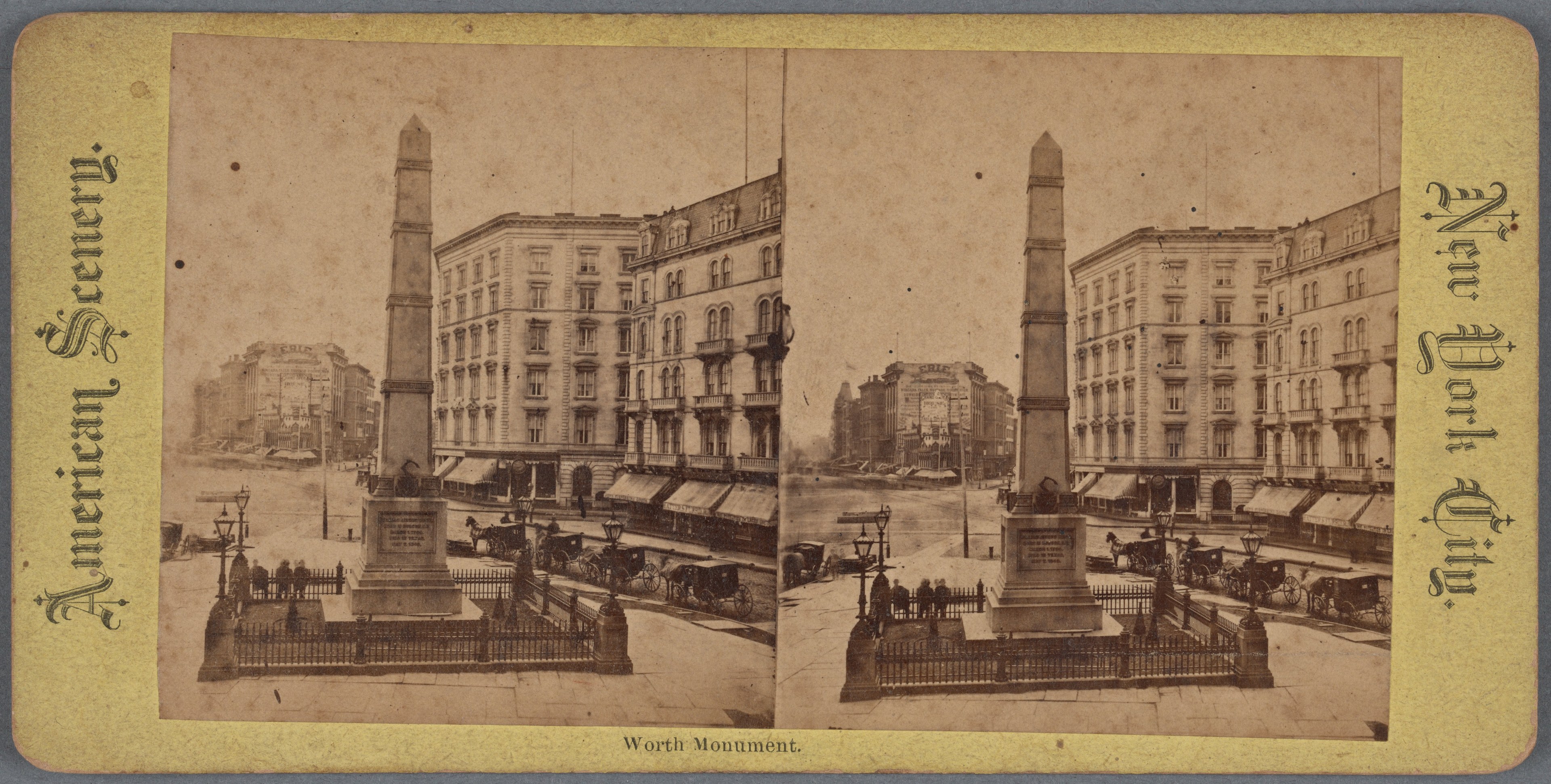 Altes Schwarz-Weiß-Foto einer Stadtstraße mit einem zentralen Denkmal, flankiert von Gebäuden, Straßeneinrichtungsgegenständen, parkenden Autos und Fußgängern auf dem Gehweg unter einem sichtbaren Himmel.