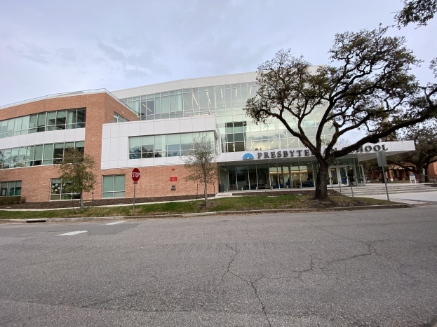 Presbyte Mittelschule, ein großes Gebäude mit vielen Fenstern, umgeben von Bäumen, Gras, Schildern, Pfosten und einer Straße, mit einem bewölkten Himmel im Hintergrund.
