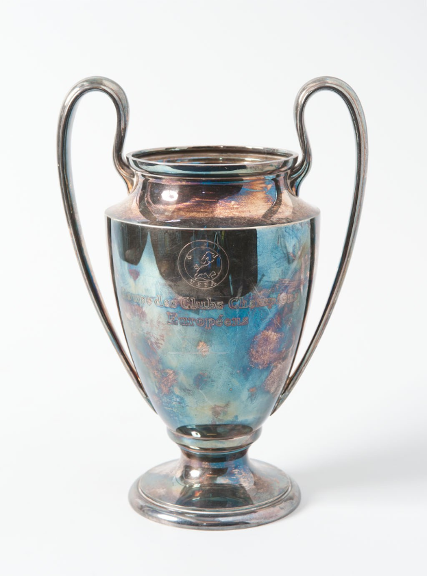 Der UEFA-Champions-League-Pokal, ein stählerner Becher mit zwei Griffen, blauen und silbernen Akzenten und der Inschrift "UEFA Champions League", vor einem weißen Hintergrund.