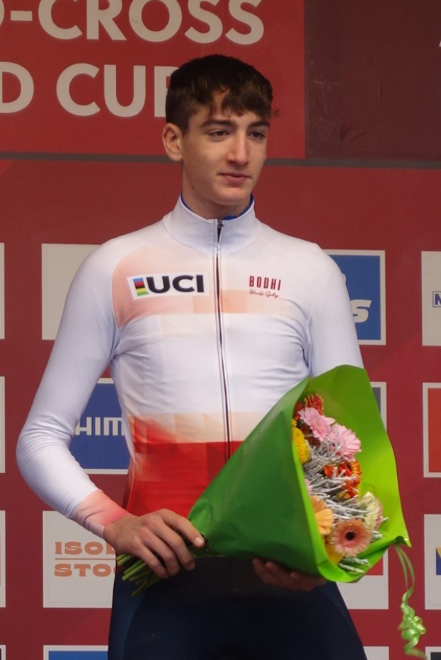 Ein Mann steht selbstbewusst auf einem Podest und hält einen Blumenstrauß, feiert einen Sieg mit einer fröhlichen Miene.