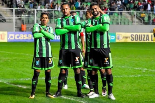 Männer in grüner und schwarzer Kleidung feiern auf einem Fußballfeld mit Zuschauern im Hintergrund.