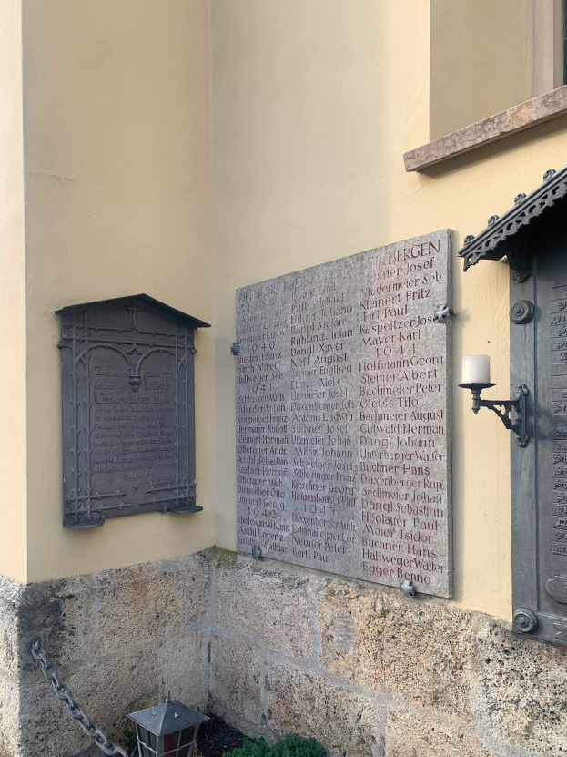 Ein Gebäude mit einer Holocaust-Gedenktafel, einem Fenster, einer Tür, einer Leuchte, einer Kette und einigen Pflanzen.