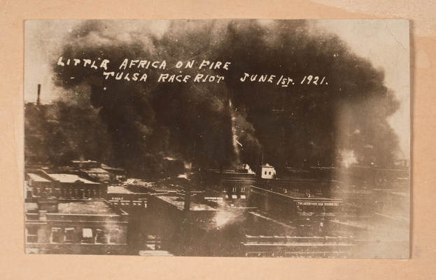 Schwarz-weiß-Foto einer Stadt mit Rauch, der aus ihrem Zentrum aufsteigt, wo Text zu sehen ist, und Gebäuden am unteren Rand, die eine belebte Stadtlandschaft andeuten.