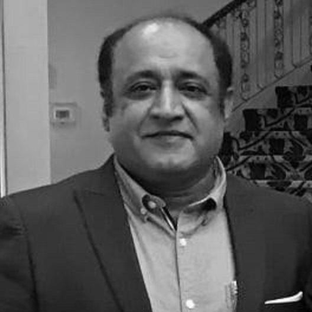 Ein Mann in einem Anzug steht vor einer Treppe und sieht besorgt aus, mit einer Wand im Hintergrund, dargestellt in Schwarz-Weiß.