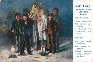 Ein Bild einer Gruppe von Menschen, die im Schnee stehen und von Laternen beleuchtet werden, mit dem Text "Mari Lwydd - Ein altes walisisches Weihnachtsbrauchtum" auf der rechten Seite.