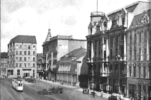 Ein Schwarz-Weiß-Foto einer Straßenansicht in Stuttgart, Deutschland, circa 1900, mit Fahrzeugen, Gebäuden mit Fenstern, Laternen und einem bewölkten Himmel.