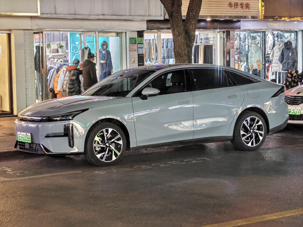 Ein Mitsubishi Lancer EV auf einer nächtlichen Stadtstraße geparkt, umgeben von Gebäuden, beleuchteten Schaufenstern, Schaufensterpuppen und Schildern.