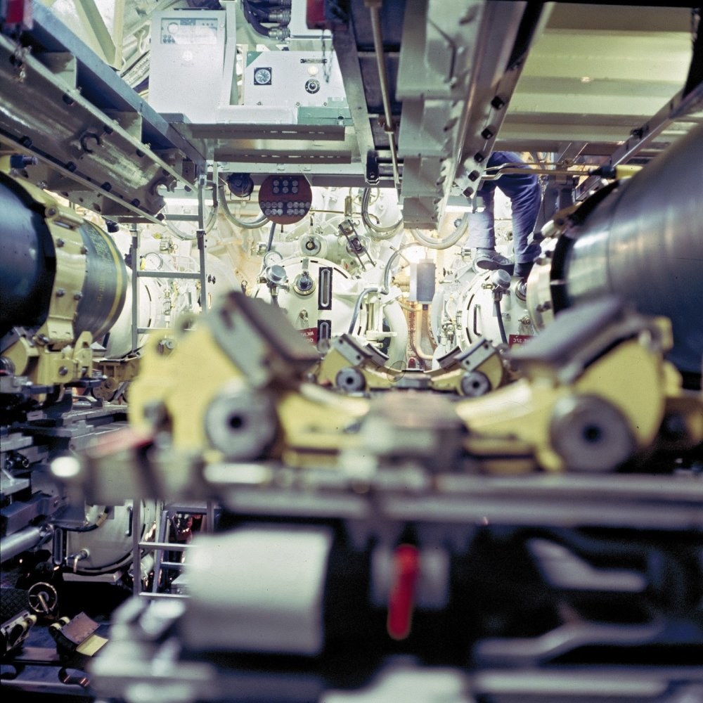 Ein Mann steht auf einer Maschine in einem industriellen Raum, umgeben von Geräten, und scheint Wartungs- oder automatisierungsbezogene Arbeit zu leisten.