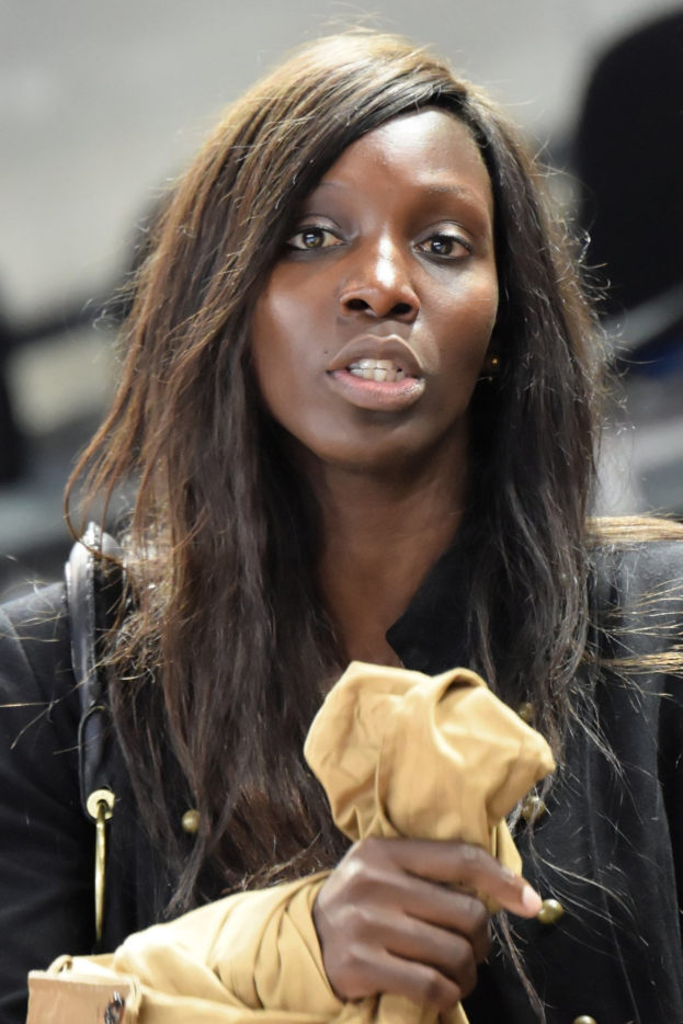 Eine selbstbewusste Frau in einem schwarzen Kleid und Handtasche hält ein Blatt Papier, ihr entschlossener Ausdruck und ihre starke Haltung deuten auf Bereitschaft für Herausforderungen hin.