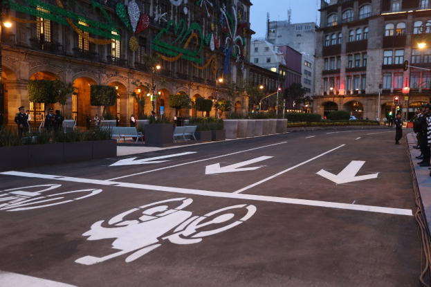Stadtstraße mit einem separaten Fahrradweg, umgeben von Gebäuden, Straßenmöbeln, Fußgängern auf dem Gehweg und Bäumen unter einem klaren blauen Himmel.