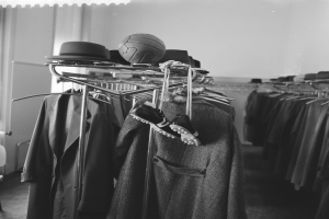 Ein Schwarz-Weiß-Foto einer Kabine mit Kleidung auf einem Ständer, Hüten und einem Ball oben drauf und einer Wand im Hintergrund.