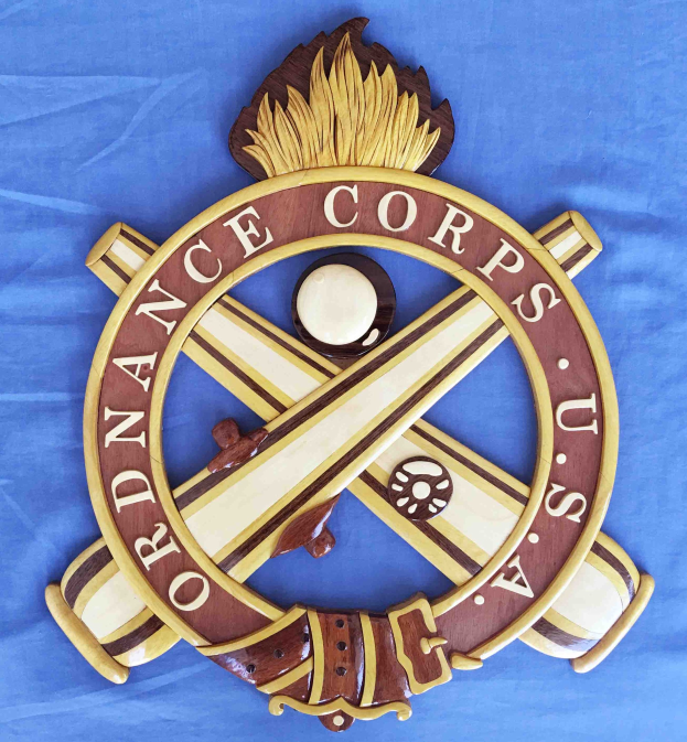 Holzschild mit "Ordnance Corps" in schwarzer Schrift, das einen weißen Stern auf einem navyblauen Hintergrund mit goldener Umrandung zeigt, auf blauem Tuch montiert.