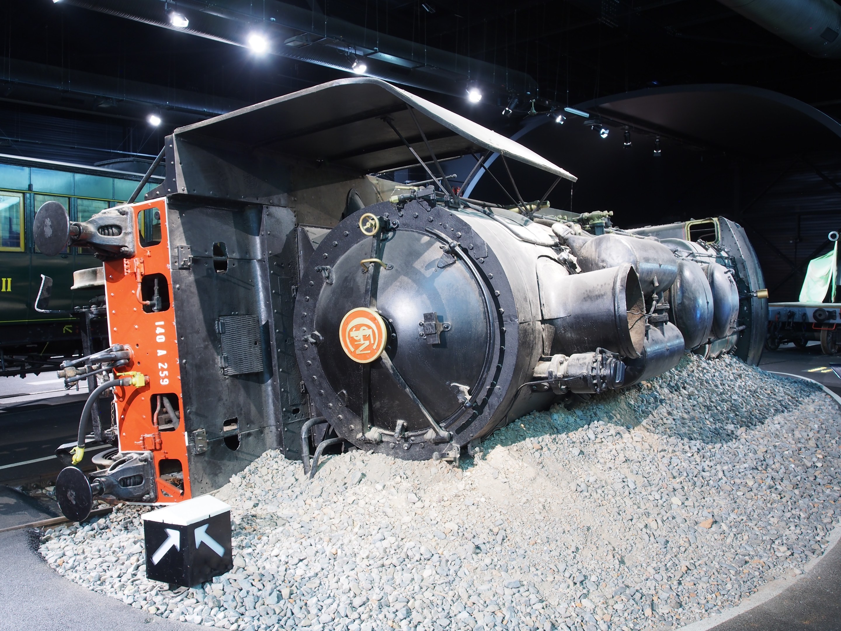 Eine alte Dampflokomotive in einem Museum ausgestellt, umgeben von Steinmauern und beleuchtet von Deckenlampen.