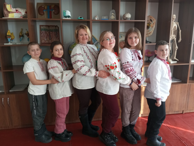Eine Gruppe von Kindern in traditioneller ukrainischer Kleidung vor einem Bücherregal mit Spielzeugen, einem Skelett und anderen Gegenständen in einer ukrainischen Schule.