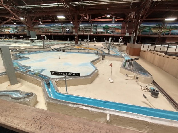 Ein großer Indoor-Wasserpark mit zahlreichen Wasserrutschen, Pfählen, Texttafeln, Deckenleuchten und Wandgemälden, der einem Minigolfplatz ähnelt.