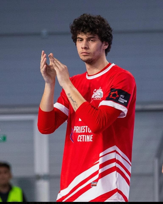 Ein Mann in einem roten und weißen Hemd klatscht in der Vordergrund, während im Hintergrund eine andere Person und eine Wand zu sehen sind, und ein Text am unteren Rand mit der Aufschrift 'Kopenhagen Futsal Club - Foto 1'.