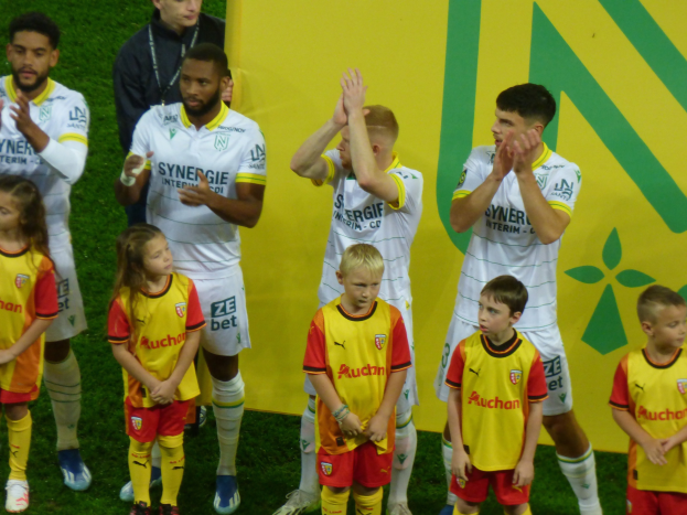 Eine Gruppe von Fußballspielern in Uniformen klatscht auf einem Ligue 1-Feld in Feierlaune, mit einem "Ligue 1"-Schild im Hintergrund.