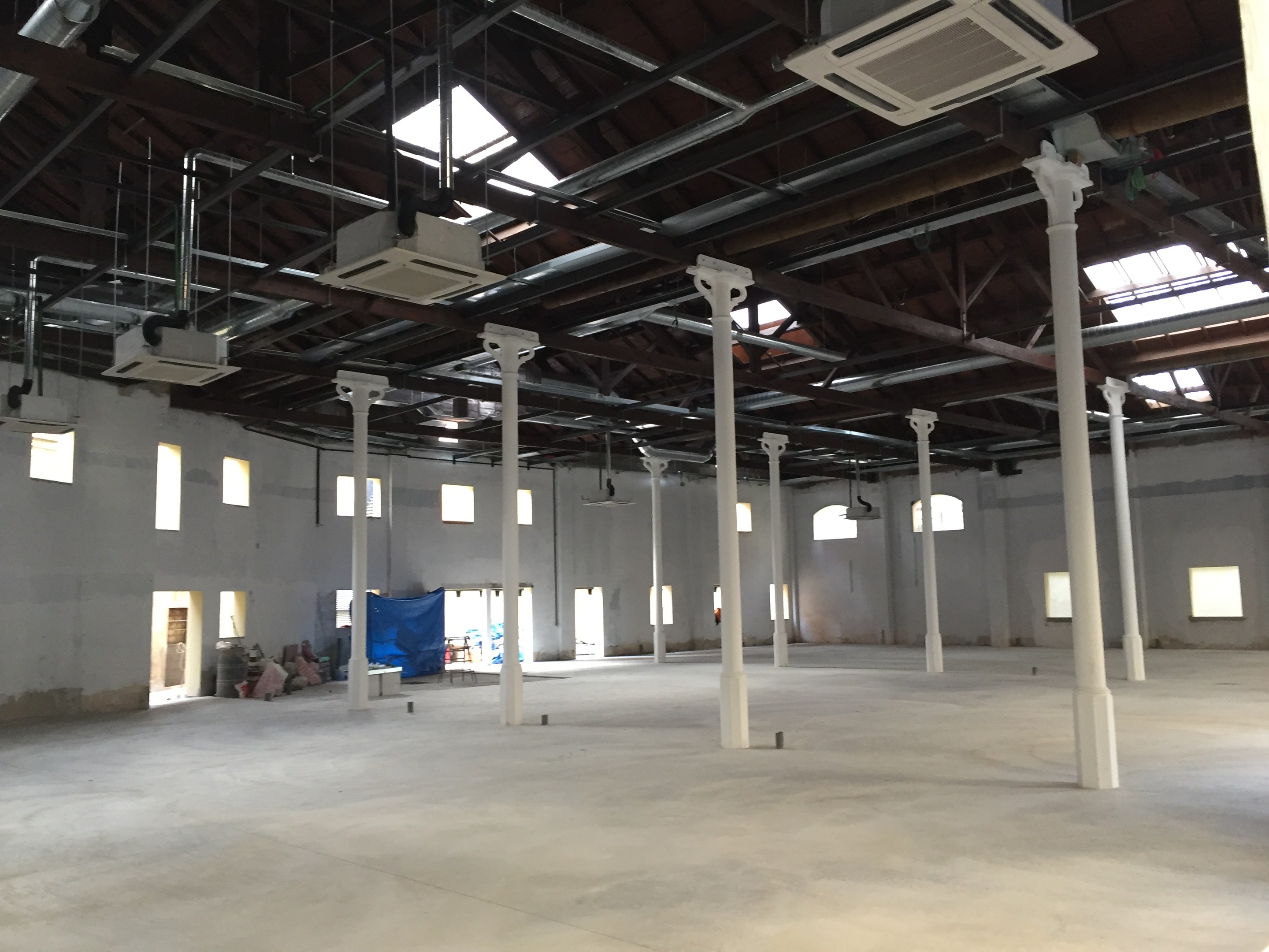 Industrielle Lagerhalle mit großen Fenstern, Säulen, Deckenleuchten, Klimaanlagen und einem offenen Grundriss zur Miete verfügbar.
