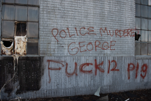 Ein Gebäude mit Graffiti, das "Polizei Mörder George Fuck 12 P19" auf der Seite trägt, mit Fenstern und diversen Gegenständen davor.