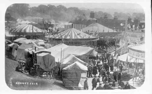 Schwarz-weiß-Foto vom Barnet Fair in London, England, mit Zelten, Menschen, Karren, Pfählen, Bäumen und Gebäuden im Hintergrund.