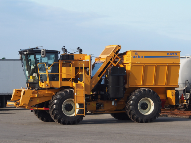 Ein großes gelbes Radlader-Modell steht vor einem weißen Container auf einer Straße mit einem klaren blauen Himmel im Hintergrund.