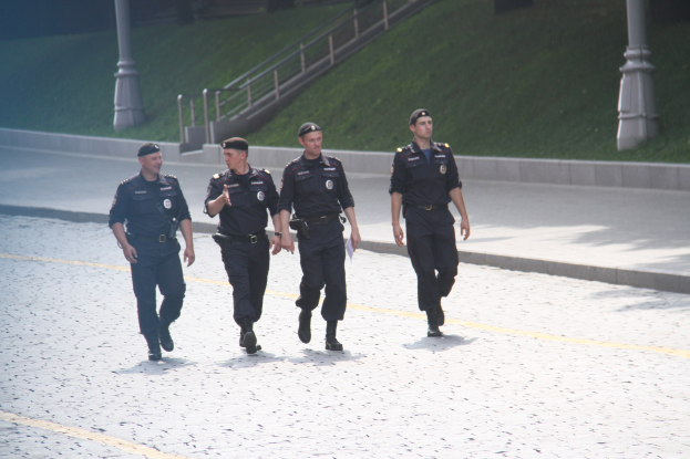 Drei Polizisten in Uniform und Mützen auf einer Straße mit Geländern, Treppen und Gras im Hintergrund.