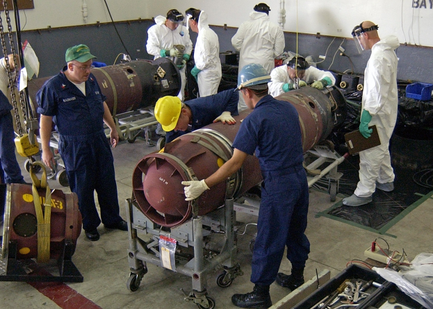 Männer in Helmen und Handschuhen, die eine große Bombe in einer Fabrik auseinandernehmen.