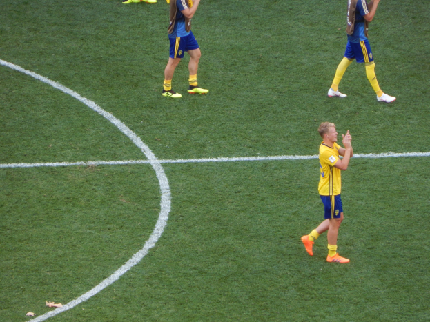 Mannergruppe in Fußballtrikots klatscht feiernd auf einem Fußballfeld.