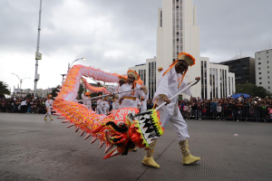 Eine Gruppe führt einen Drachen Tanz mit kostümierten Teilnehmern auf, die Stöcke halten, während Zuschauer vor Gebäuden und Bäumen zuschauen, während sie das chinesische Neujahrsfest in Brisbane feiern.