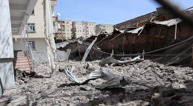 Die Auswirkungen eines israelischen Luftangriffs in Gaza-Stadt, der ein zerstörtes Gebäude zeigt, das zu Schutt und Asche geworden ist, auf einer Straße, mit eingestürzten Wänden, Metallstangen, einem Zaun, einer Treppe, nahen Gebäuden, Bäumen und einem bewölkten Himmel.