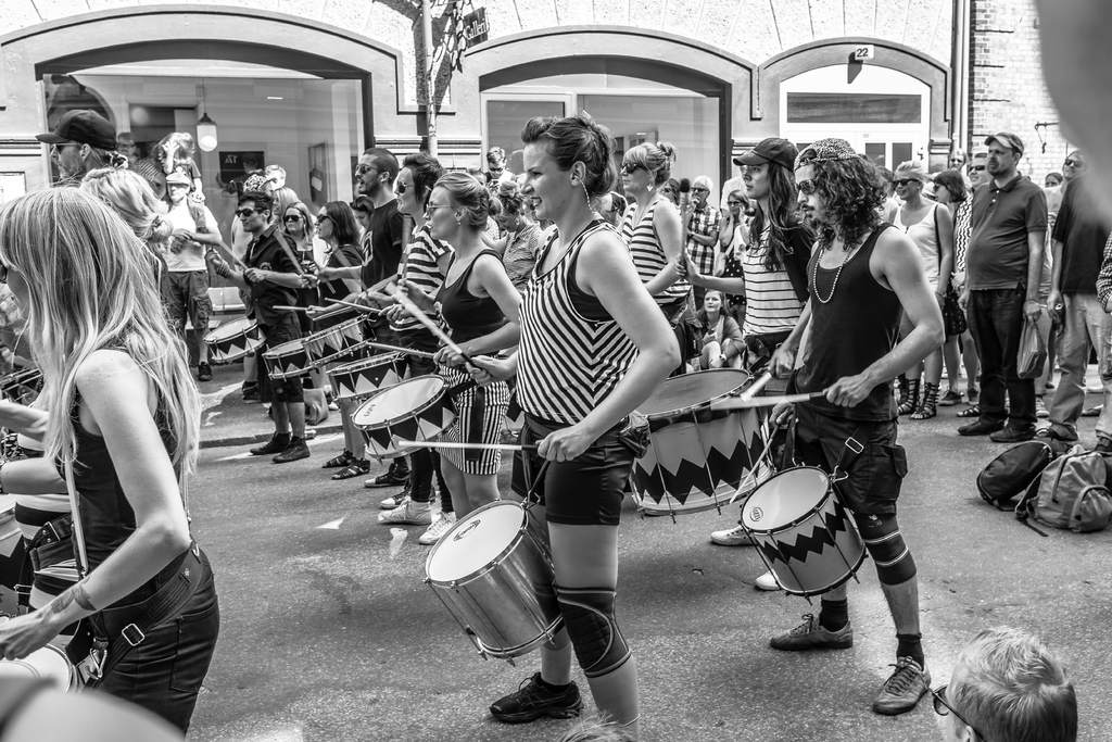 Eine Gruppe von Menschen, die draußen Musikinstrumente spielen, mit einer geschlossenen Glastür und einer Leuchte im Hintergrund.