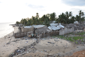 Ein Strand in den Philippinen mit verstreuter Plastikmüll, Hütten, Bäumen und einem Gewässer, unter einem sichtbaren Himmel.