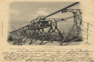 Ein altes Schwarz-Weiß-Foto einer Eisenbahnbrücke mit einem Kran, umgeben von Bäumen und einem bewölkten Himmel, mit dem Text "Bahnstrecke, die erste Eisenbahnbrücke in Deutschland" unten.