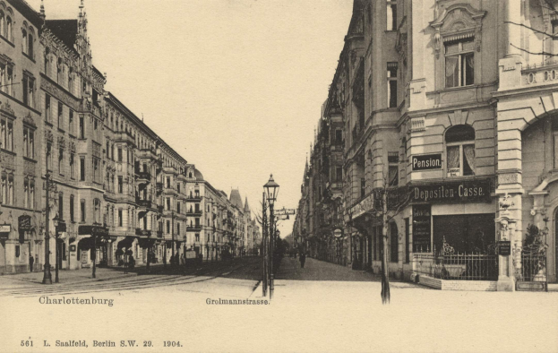 Schwarz-weiß-Foto einer Straße in Charlottenburg, Deutschland, mit Gebäuden, Straßenmasten, Lichtern, Namensschildern, Kraftfahrzeugen, Füßgängern, Gittern und einem klaren Himmel.