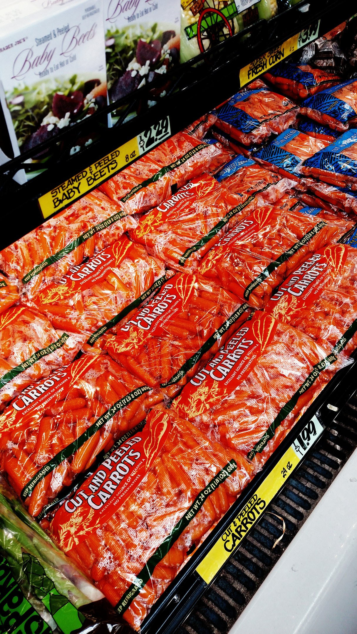 Vitrine eines Supermarkts mit verschiedenen verpackten Lebensmitteln, darunter Gemüsepackungen, jeweils mit angebrachten Preisschildern.