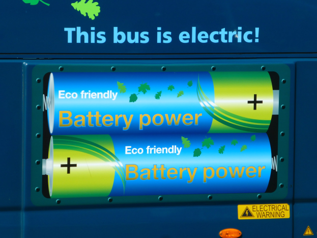 Ein blauer Elektrobus mit der Aufschrift "Dieser Bus ist elektrisch" und zwei sichtbaren seitlich angebrachten Batterien.
