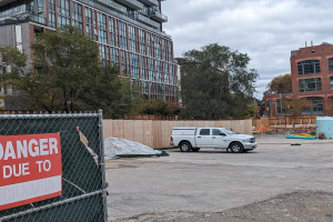 Truck parked near a building with a "Danger Due to Open Excavation" sign, trees, buildings, poles, and a clear blue sky in the background.