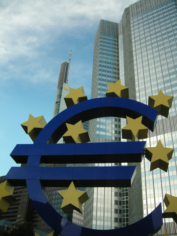 Das Euro-Zeichen steht vor dem Hauptquartier der Europäischen Zentralbank, einem großen modernen Gebäude, das von Bäumen umgeben ist.