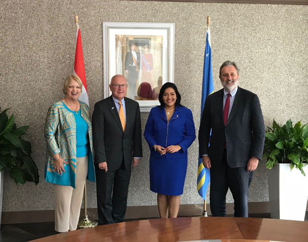 Eine Gruppe strahlender Menschen um einen Tisch mit Papieren herum, umgeben von Fahnen, Topfpflanzen und einem Foto auf der Wand, feiert die Unterzeichnung eines Memorandums von Verständnis zwischen den Vereinigten Staaten und Kanada.