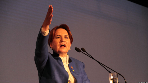 Eine Frau steht an einem Podium mit einem Glas Wasser und zwei Mikrofonen und hält eine Rede vor einem Bildschirm, wahrscheinlich zu einer Regierungsentscheidung, Frauenrechte zu verbieten.