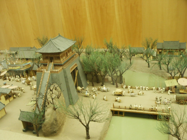 Ein Miniaturmodell eines chinesischen Dorfes in einem Museum, das Häuser, Bäume, Menschen, Tiere, eine Brücke, einen Felsen und eine hölzerne Wand enthält.