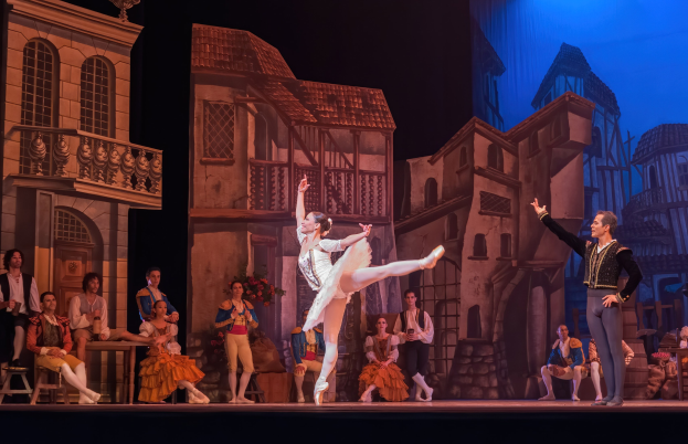 Zwei Tänzer performen auf einer Bühne im Royal Opera House in London, mit einem Publikum, das im Hintergrund sitzt und steht.