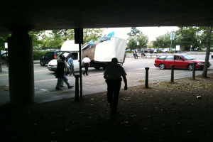 Eine belebte Straßenszene mit zahlreichen Fußgängern, einem Auto und einem Lastwagen auf der Straße.