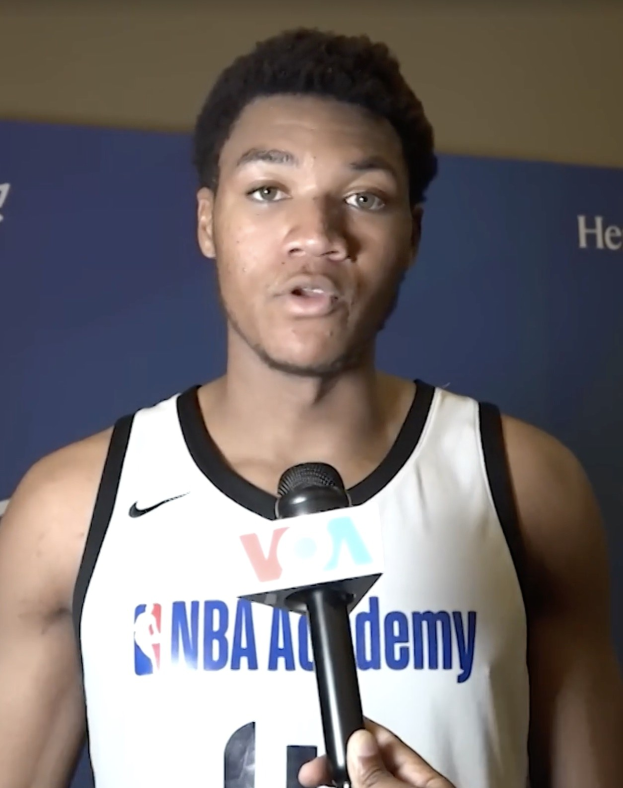 Ein Mann in einem wei\uen Tanktop h"alt ein Mikrofon und spricht mit der Presse auf der NBA All-Star-Game 2019, mit einem Banner und einer Wand im Hintergrund.