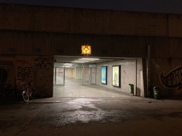 Leerer Parkplatz in der Nacht mit Graffiti an den Wänden, ein Fahrrad davor geparkt und ein naher Müllcontainer; Rahmenleuchten säumen die Wände, der Himmel ist im Hintergrund zu sehen.