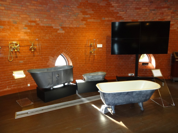 Ein gemütliches Badezimmer mit einer Backsteinwand, einer zentralen Badewanne, an der Wand montierten Hähnen auf der linken Seite und einem an der Wand montierten Fernseher auf der rechten Seite.