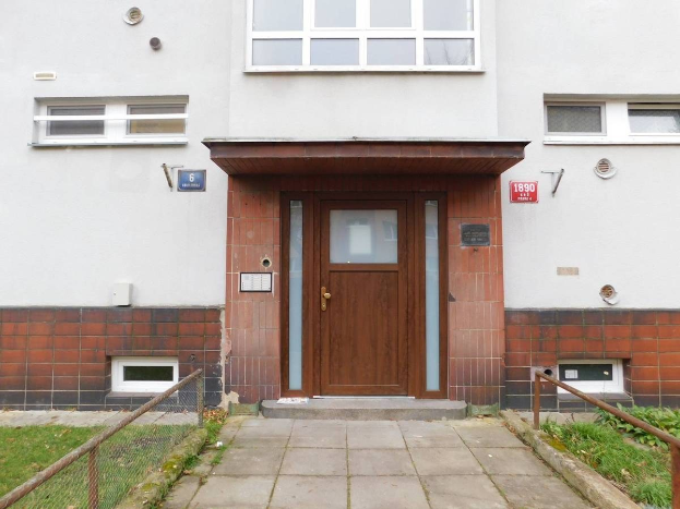 Zwei Schlafzimmer großes Reihenhaus mit weißer Fassade, brauner Tür und Fenstern, Metallzaun, Gras, Weg und Brettern an der Wand zum Verkauf in St Johns Court, St Johns Road, Luton.